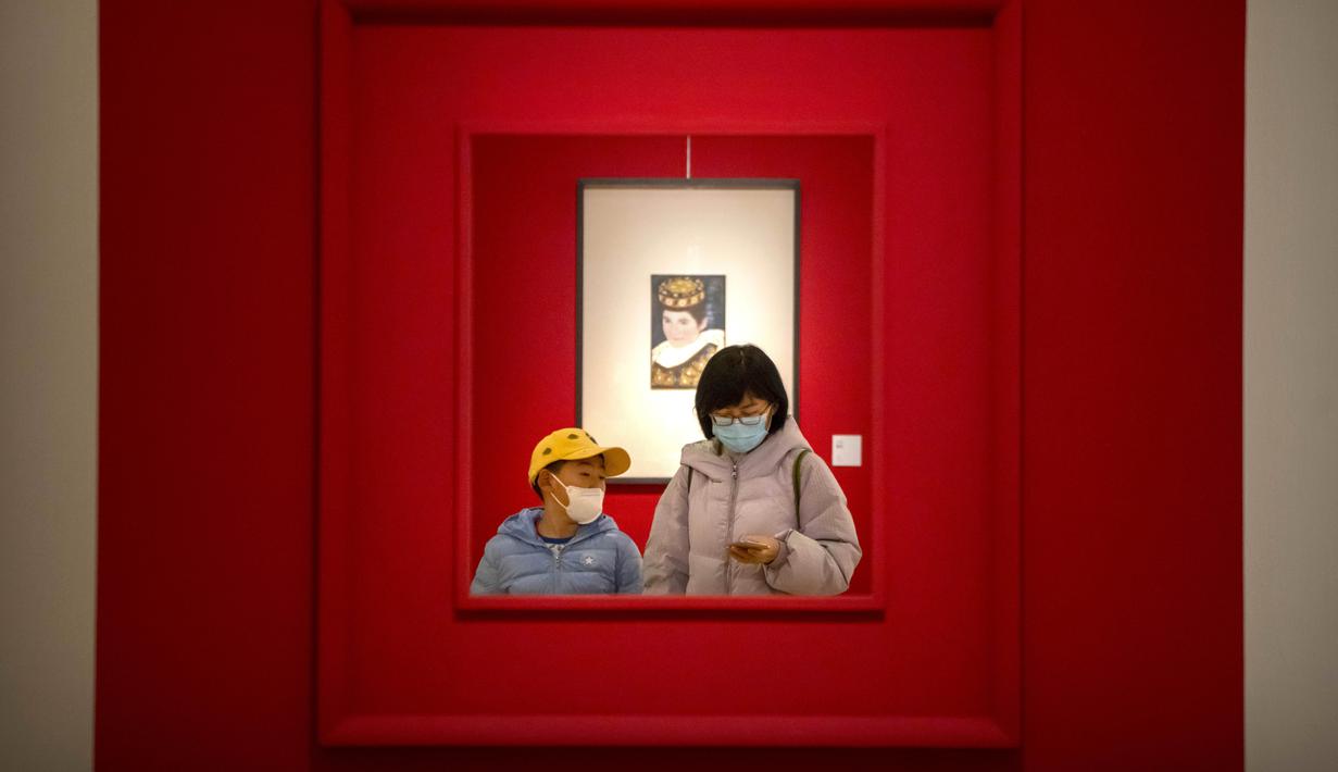 Seorang wanita dan anak mengenakan masker berjalan melalui galeri di Museum Seni Nasional China di Beijing, Rabu (1/2/2023). Pengunjung terus berduyun-duyun ke museum, situs bersejarah, dan tempat wisata di ibu kota China saat periode liburan Tahun Baru Imlek berakhir. (AP Photo/Mark Schiefelbein)