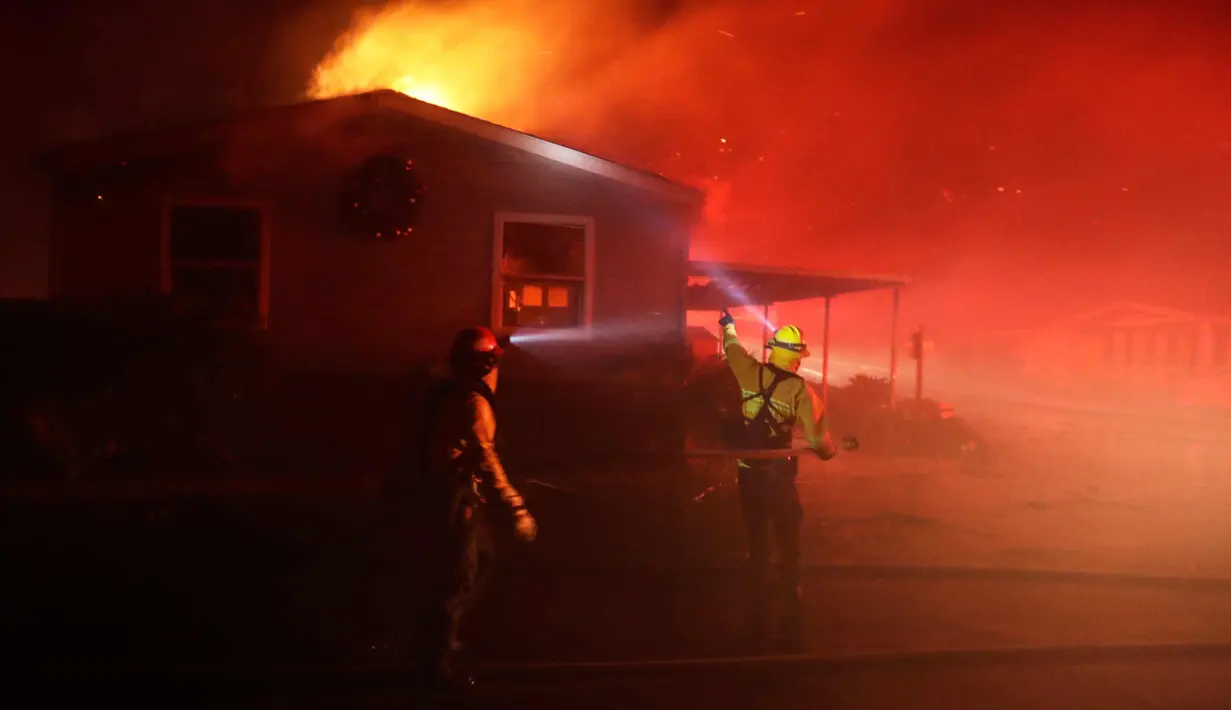 Dua petugas berusaha memadamkan api yang membakar sebuah rumah di Fallbrook, California (7/12). Dipicu oleh angin kencang Santa Ana, api merambat dengan cepat dan merusak puluhan rumah di Southern California. (AP Photo / Gregory Bull)