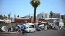 Seorang pengendara sepeda melewati orang-orang yang sedang berkemah di "The Zone", perkemahan tunawisma yang luas tempat ratusan orang tinggal, selama rekor gelombang panas di Phoenix, Arizona, pada 18 Juli 2023. (Patrick T. Fallon / AFP)
