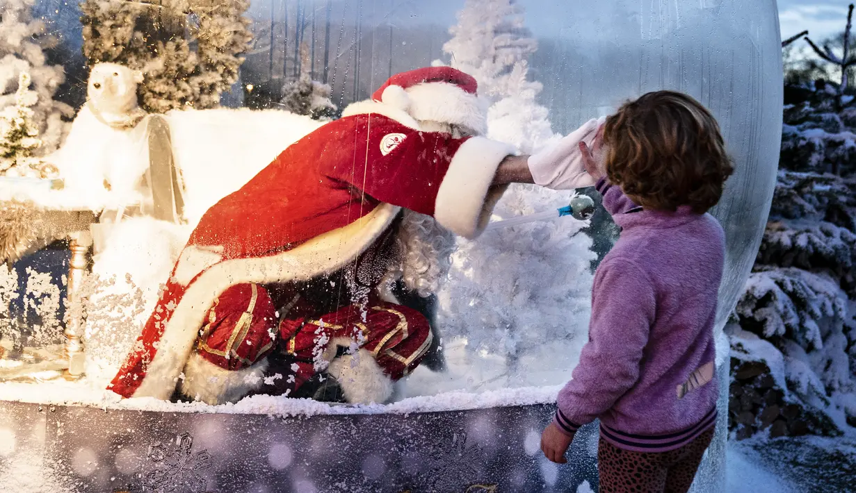 Seseorang yang berpakaian seperti Sinterklas yang berada dalam bola salju seukuran aslinya bertemu dengan anak-anak saat membuka musim Natal di Kebun Binatang Aalborg, di tengah krisis virus corona yang berlanjut, di Aalborg, Denmark pada Jumat (13/11/2020). (Henning Bagger / Ritzau Scanpix / AFP)