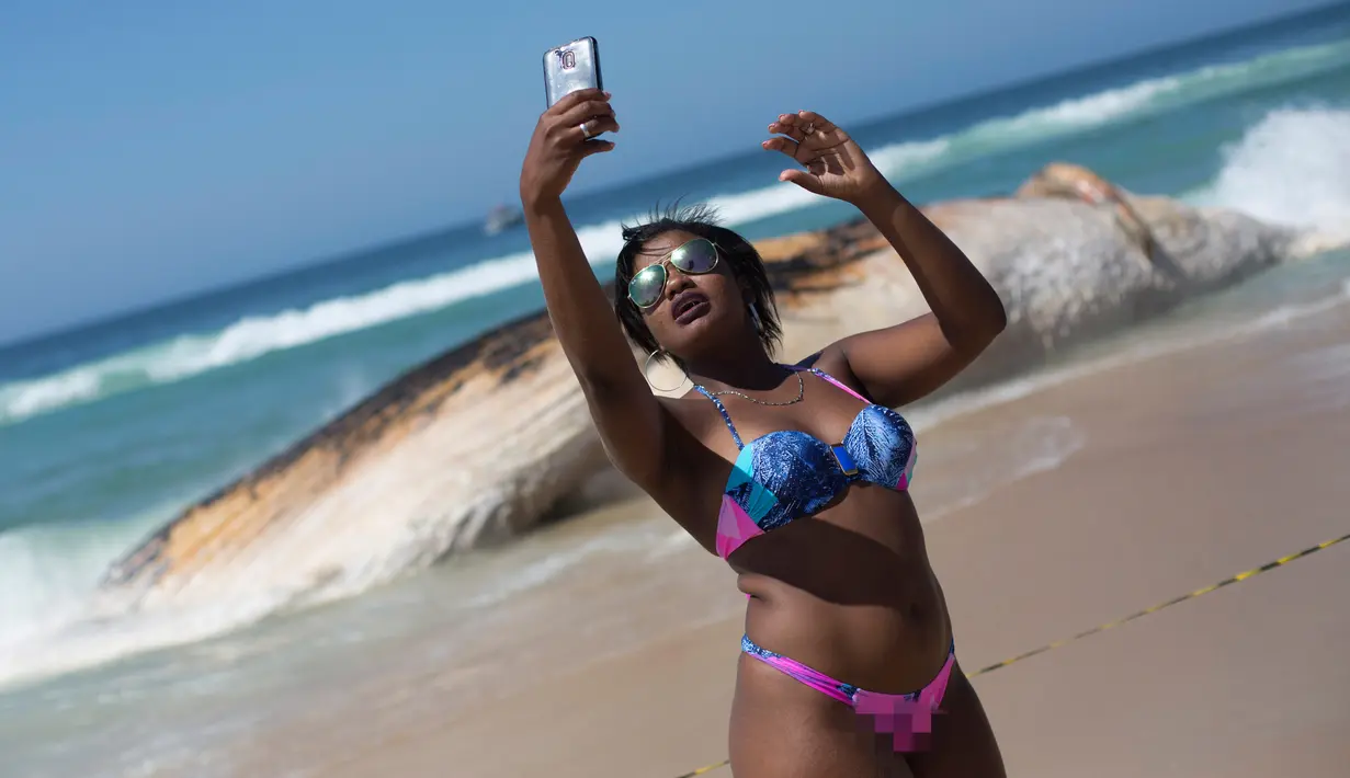 Pengunjung berswafoto dengan latar belakang bangkai paus di tepi pantai Ipanema, Rio de Janeiro, Rabu (15/11). Bangkai paus itu sempat mengejutkan pengunjung yang sedang berenang di pantai yang termasuk paling ramai di Brasil. (AFP PHOTO / Leo Correa)