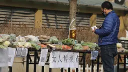 Seorang pria membeli sayuran di kios sayur tak berpenjaga di permukiman di Shijiazhuang, Provinsi Hebei, China utara (12/2/2020). Kios sayur tak berpenjaga itu didirikan untuk menyediakan sayuran kepada warga dengan kontak minimal sebagai upaya melawan epidemi virus corona. (Xinhua/Liang Zidong)