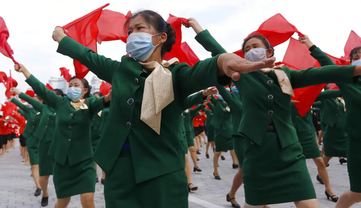 Wanita yang mengenakan masker wajah untuk membantu mengekang penyebaran virus corona COVID-19 berparade dengan bendera saat rapat umum menyambut Kongres ke-8 Partai Buruh Korea di Lapangan Kim Il Sung, Pyongyang, Korea Utara, Senin (12/10/2020). (AP Photo/Jon Chol Jin)