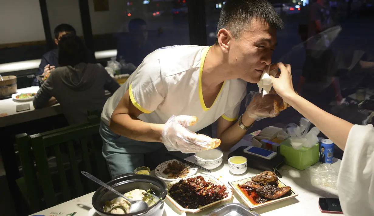 Pengunjung menyeka mulut rekannya saat menikmati hidangan kepala kelinci di sebuah restoran di Chengdu, ibu kota Provinsi Sichuan di barat daya China, 8 September 2016. Di sini, otak kelinci menjadi menu favorit warga lokal maupun asing. (WANG ZHAO/AFP)