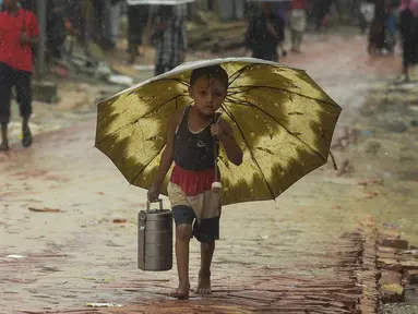 Seorang anak pengungsi Rohingya berjalan membawa rantang selama musim hujan di kamp pengungsi Kutupalong, Ukhia (12/9/2019). Kamp ini adalah salah satu dari dua kamp pengungsi yang dikelola pemerintah di Cox's Bazar, kamp yang satunya lagi adalah kamp pengungsi Nayapara. (AFP Photo/Munir Uz Zaman)