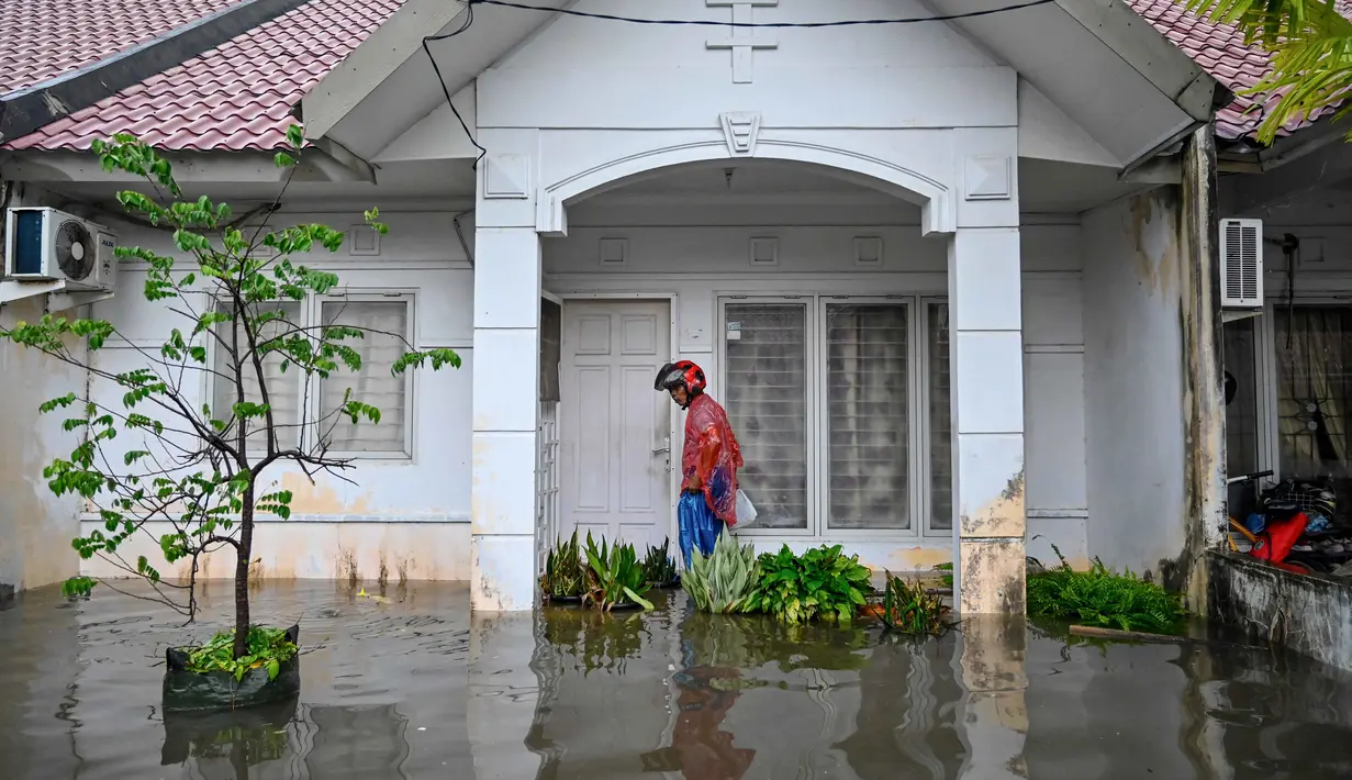 Badan Penanggulangan Bencana Daerah (BPBD) Aceh Besar mengimbau masyarakat untuk tetap waspada terhadap potensi banjir susulan, mengingat kondisi hujan masih berpotensi terjadi. Tampak dalam foto, seorang pria memeriksa rumahnya yang terendam banjir setelah hujan deras di permukiman Darul Imarah, pinggiran Banda Aceh, pada Kamis 27 November 2025. (CHAIDEER MAHYUDDIN/AFP)