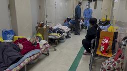 Seorang pria berbicara dengan pekerja medis ketika pasien lanjut usia beristirahat di sepanjang koridor bangsal darurat untuk menerima infus di sebuah rumah sakit di Beijing, Kamis (5/1/2023). Pasien, kebanyakan dari mereka lansia, berbaring di tandu di lorong dan menerima oksigen sambil duduk di kursi roda saat kasus COVID-19 melonjak di ibu kota China, Beijing. (AP Photo/Andy Wong)