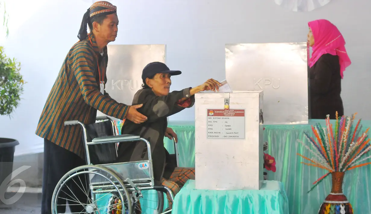 Warga disabilitas dibantu petugas KPPS berpakaian tradisional khas Jawa dan blangkon saat mengikuti pencoblosan Pilkada DKI 2017 di TPS tempat Presiden Jokowi menggunakan hak suaranya, TPS 04 Gambir, Jakarta Pusat, Rabu (15/2). (Liputan6.com/Angga Yuniar)