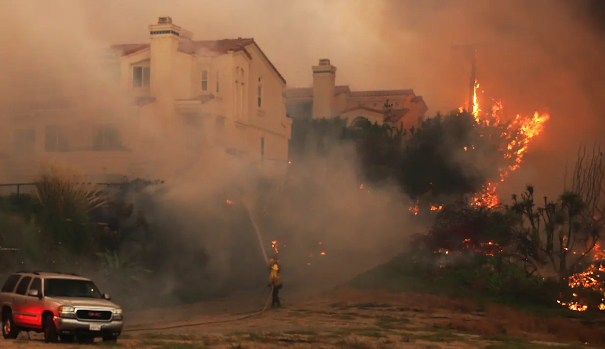 Petugas pemadam kebakaran berjuang memadamkan kobaran api di Pacific Coast Highway, Malibu, California, AS, Jumat (9/11). Api Woolsey menjalar ke jalan raya dan menuju kota pesisir, termasuk kawasan wisata Malibu dan Calabasas. (AP Photo/Reed Saxon)