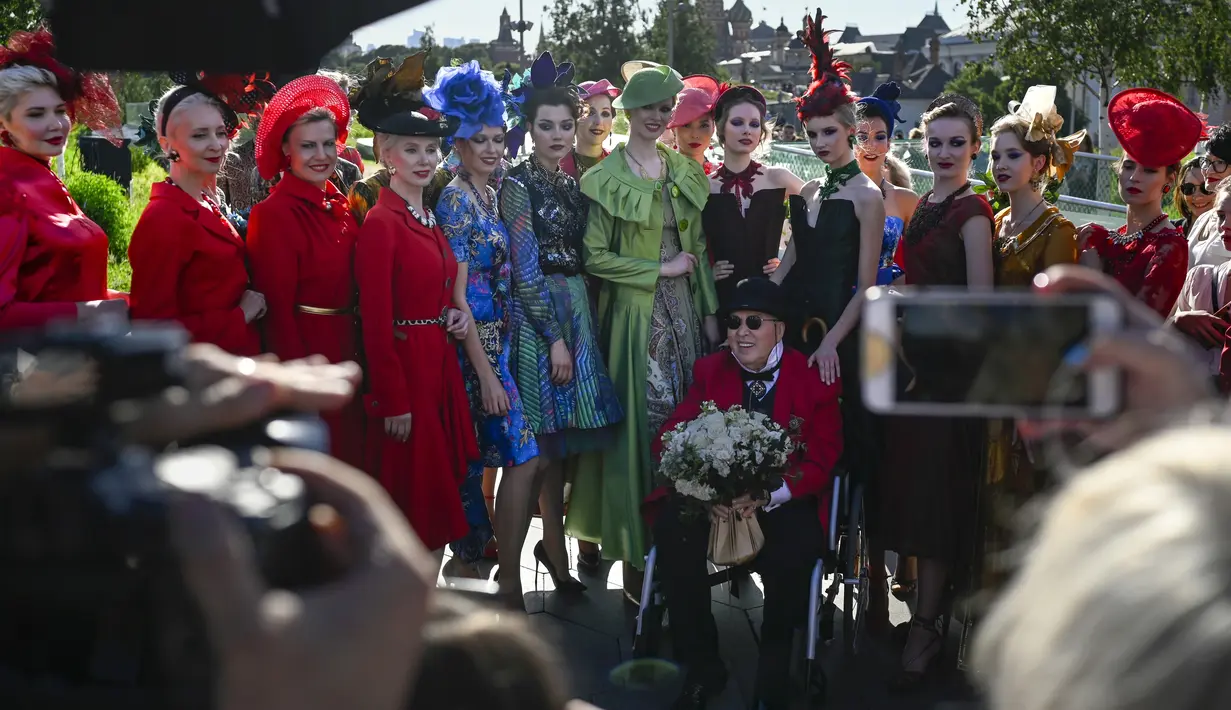 Desainer Rusia Slava Zaitsev (tengah bawah) berpose dengan model setelah menampilkan koleksinya selama pembukaan Fashion Week di Zaryadye Park dengan Katedral St. Basil sebagai latar belakang dekat Lapangan Merah di Moskow, Rusia, Senin (20/6/2022). (AP Photo)
