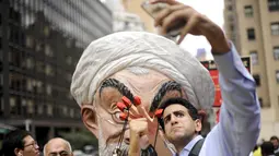 Seorang pria berselfie dengan Max Saatchi yang memakai topeng Presiden Iran Hassan Rouhani mengecam pelanggaran hak asasi manusia oleh pemerintah Rouhani di luar markas besar PBB, Manhattan, New York, AS (28/9/2015). (REUTERS/Darren Ornitz)