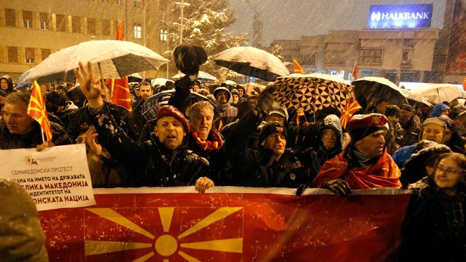 Warga membentangkan bendera Macedonia saat menggelar protes di depan gedung Parlemen, Skopje, Selasa (27/2). Di tengah hujan salju dan temperatur ekstrem, mereka turun ke jalan memprotes wacana pengubahan nama negara mereka. (AP/Boris Grdanoski)