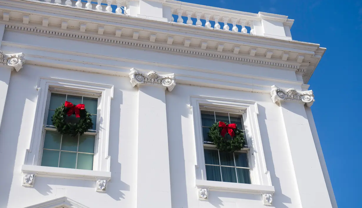 Karangan bunga Natal tergantung di jendela Gedung Putih, Washington DC, Senin (27/11). First Lady Melania Trump mendekorasi perayaan Natal dengan tema 'Time-Honored Traditions' yang mencerminkan tradisi liburan 200 tahun di Gedung Putih. (SAUL LOEB / AFP)