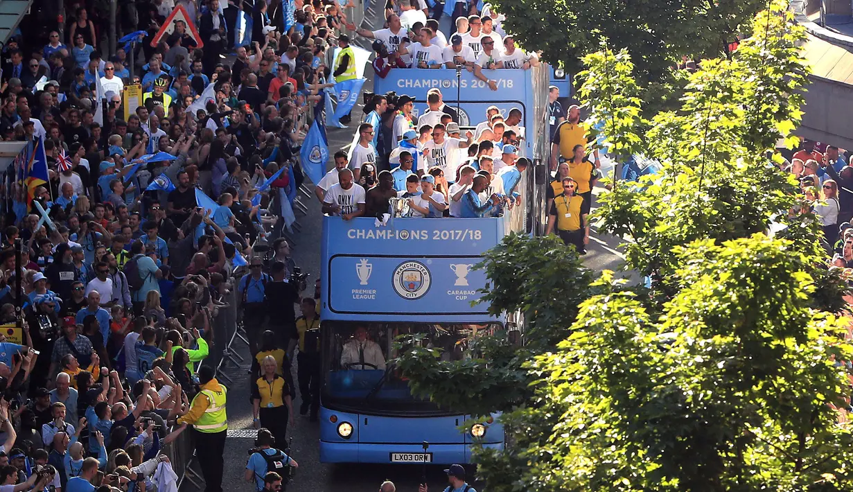 Pemain Manchester City melambaikan tangan dari atas bus beratap terbuka saat parade merayakan keberhasilan menjadi juara Liga Primer Inggris di Manchester, Senin (14/5). Sekitar 100 ribu fans ManCity membirukan Kota Manchester. (Danny Lawson/PA via AP)