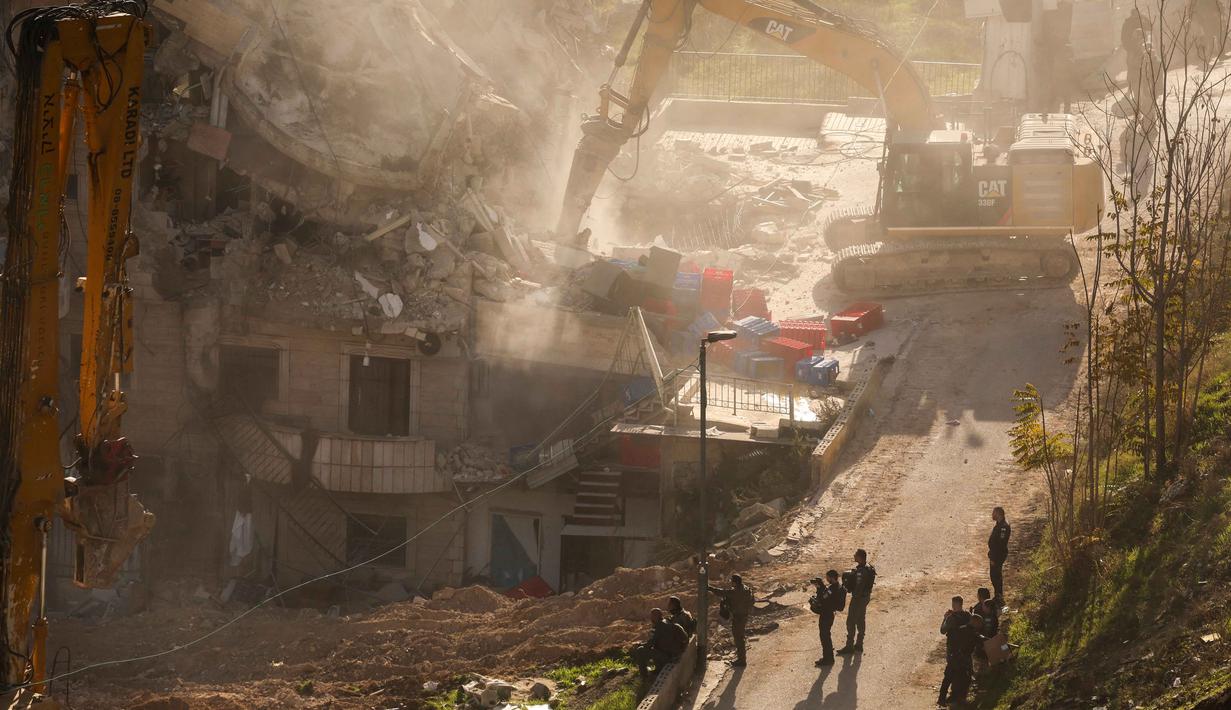 Otoritas Israel mengklaim bangunan tersebut didirikan tanpa izin bangunan yang sah. Tampak dalam foto, pasukan Israel berkumpul saat sebuah ekskavator merobohkan sebuah bangunan yang dibangun tanpa izin di lingkungan Wadi Qaddum, Yerusalem timur, pada Senin 22 Desember 2025. (Ahmad GHARABLI/AFP)