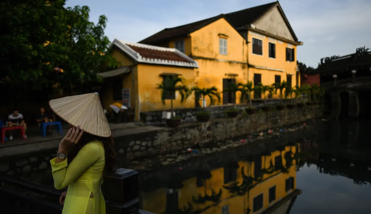 Gambar pada 14 September 2019 menunjukkan seorang turis mengenakan pakaian tradisional Vietnam ketika berpose di kota tua Hoi An. Kota Tua Hoi An merupakan destinasi wisata yang cukup populer di Vietnam, didukung oleh statusnya sebagai salah satu Unesco World Heritage Site. (Manan VATSYAYANA/AFP)