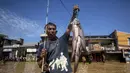 Air merendam permukiman hingga jalan raya dengan ketinggian beragam. Tampak dalam foto, seorang pria menunjukkan ikan tangkapannya saat memancing di jalanan Bandung yang tergenang banjir, Jawa Barat, pada Jumat 5 Desember 2025. (TIMUR MATAHARI/AFP)