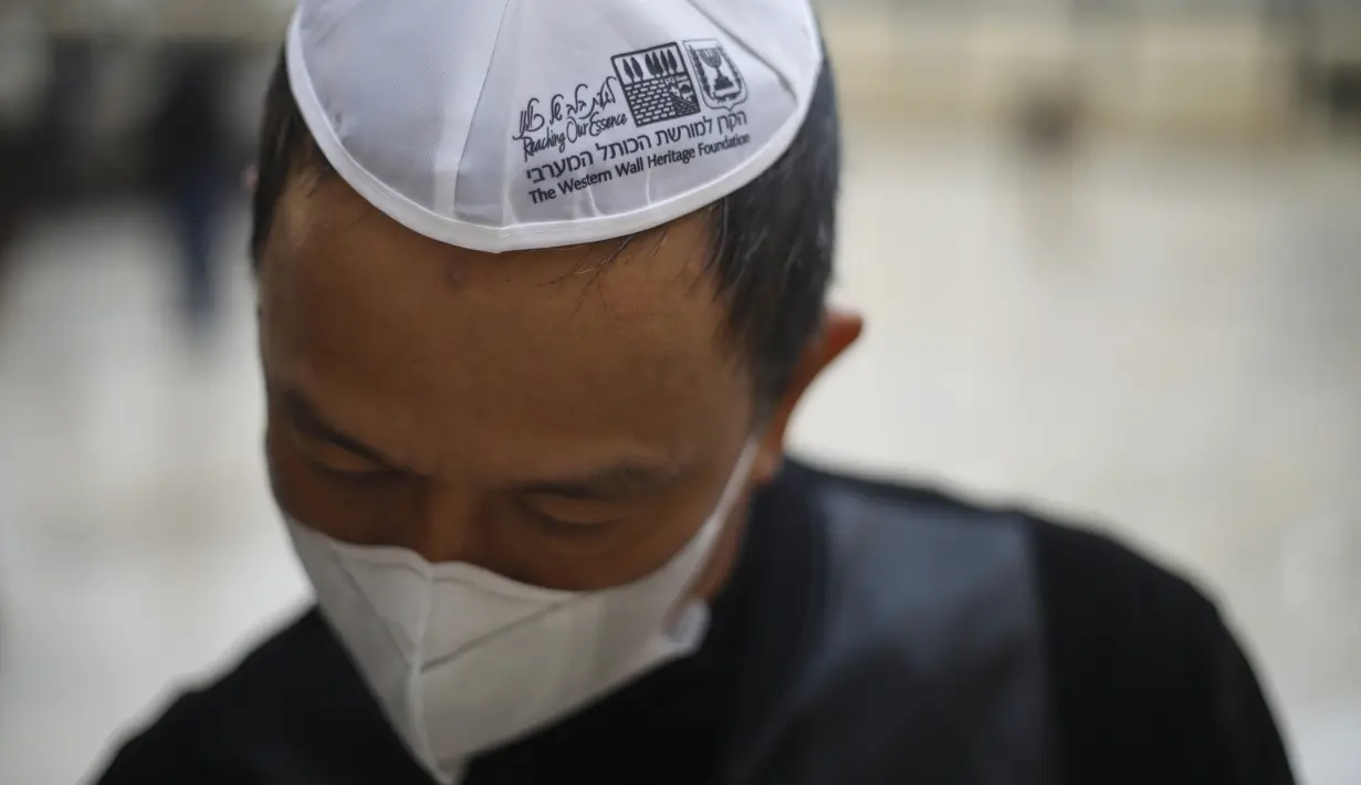 Seorang pria mengenakan masker berdoa di Tembok Ratapan di Kota Tua Yerusalem (16/2/2020). Ketika kekhawatiran tentang penyebaran virus corona meningkat, umat Yahudi yang setia mengadakan sesi doa untuk mencari intervensi ilahi untuk membantu mencegah penyakit tersebut. (AP Photo/Ariel Schalit)