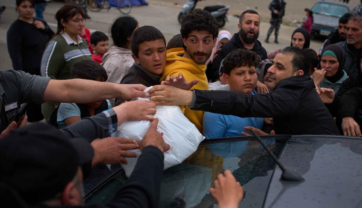 Di sisi lain, Kementerian Kesehatan Lebanon, pada Jumat 27 Maret 2026, melaporkan jumlah korban tewas akibat serangan Israel sejak 2 Maret 2026 telah mencapai 1.142 jiwa. Sementara, 3.315 orang lainnya terluka. Tampak dalam foto, para pengungsi yang melarikan diri dari serangan artileri Israel di Lebanon selatan meraih kantong-kantong makanan selama pembagian di samping tenda-tenda yang digunakan sebagai tempat penampungan di Beirut, Lebanon, Rabu, 1 April 2026. (AP Photo/Emilio Morenatti)