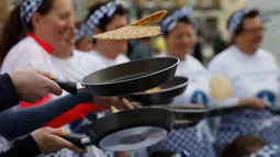 Peserta melemparkan pancake mereka sebelum mengambil bagian dalam lomba lari sembari membawa wajan di Olney, Buckinghamshire, Inggris, Selasa (25/2/2020). Para peserta kompetisi tahunan tersebut harus membolak-balikan pancake sambil tetap berlari. (AP/Alastair Grant)