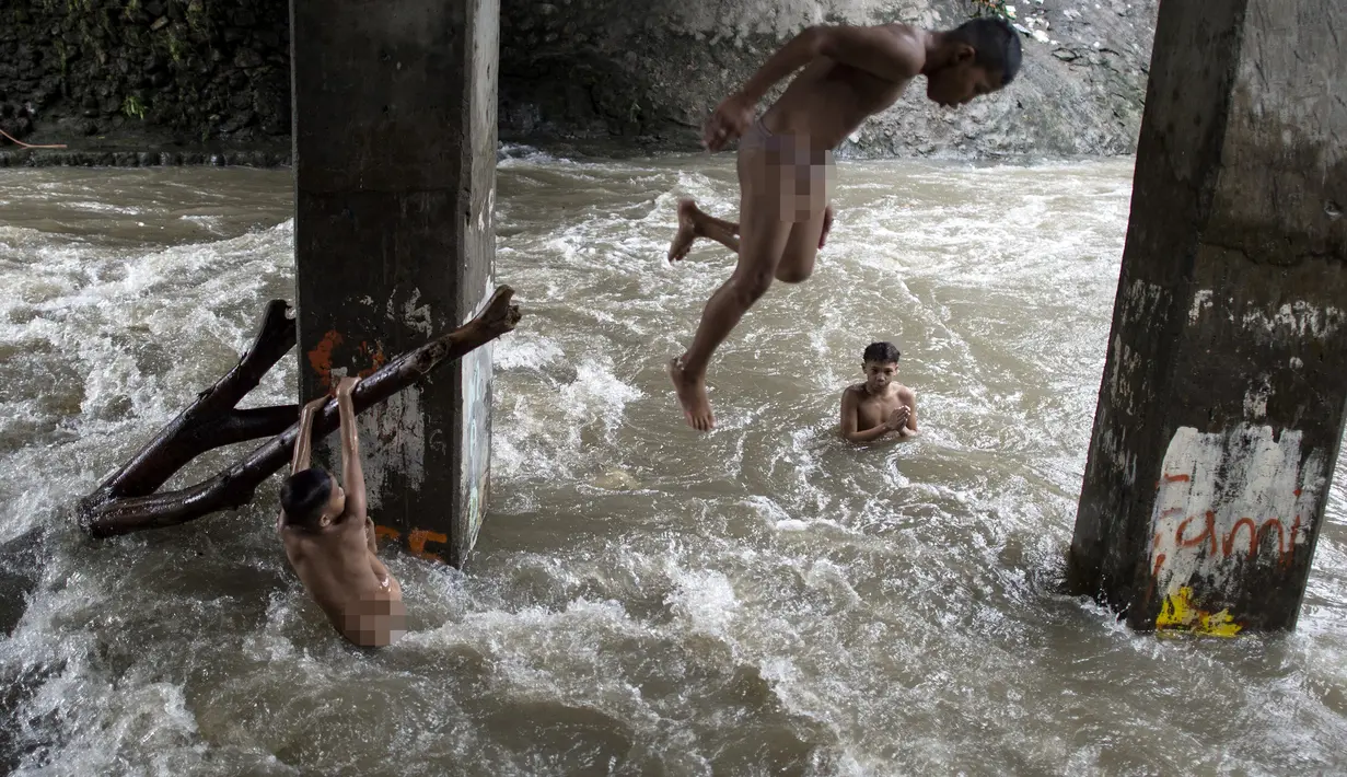 Sejumlah anak bermain di sungai dengan arus yang sangat deras akibat hujan lebat di bawah jembatan di Manila, Filipina (11/6). (AFP Photo/Noel Celis)