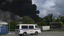 Asap hitam dari kebakaran besar di depot bahan bakar terlihat saat sebuah truk air melewati jalan di Matanzas, Kuba (7/8/2022). Kuba meminta bantuan Sabtu (7/7) untuk mengatasi kebakaran besar yang menyebabkan 77 orang terluka dan 17 petugas pemadam kebakaran hilang. Sekitar 800 orang telah dievakuasi dari daerah tersebut. (AFP/Yamil Lage)