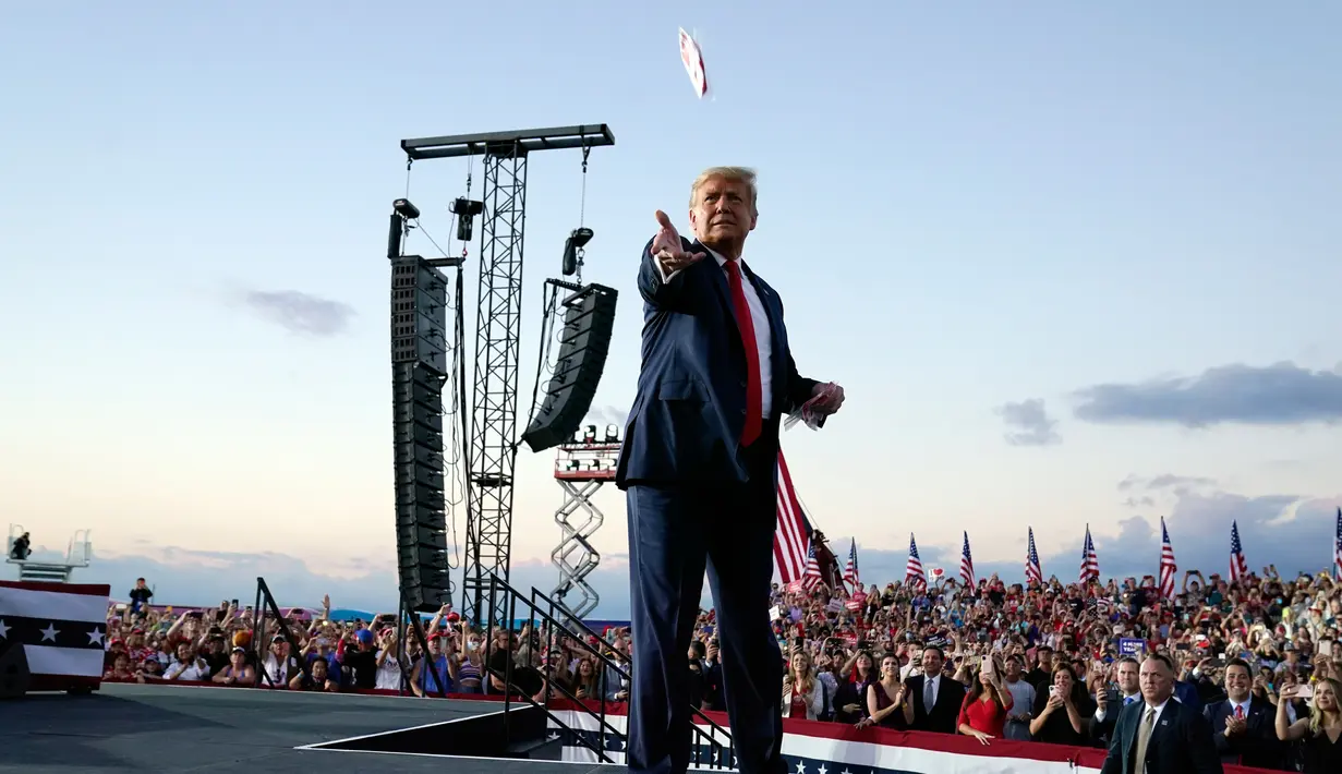 Presiden Donald Trump melemparkan masker dari atas panggung ke kerumunan pendukung saat berkampanye di Bandara Internasional Orlando Sanford di Sanford, Florida, Senin (12/10/2020). Donald Trump kembali berkampanye untuk pertama kalinya usai dinyatakan negatif Covid-19. (AP Photo/Evan Vucci)