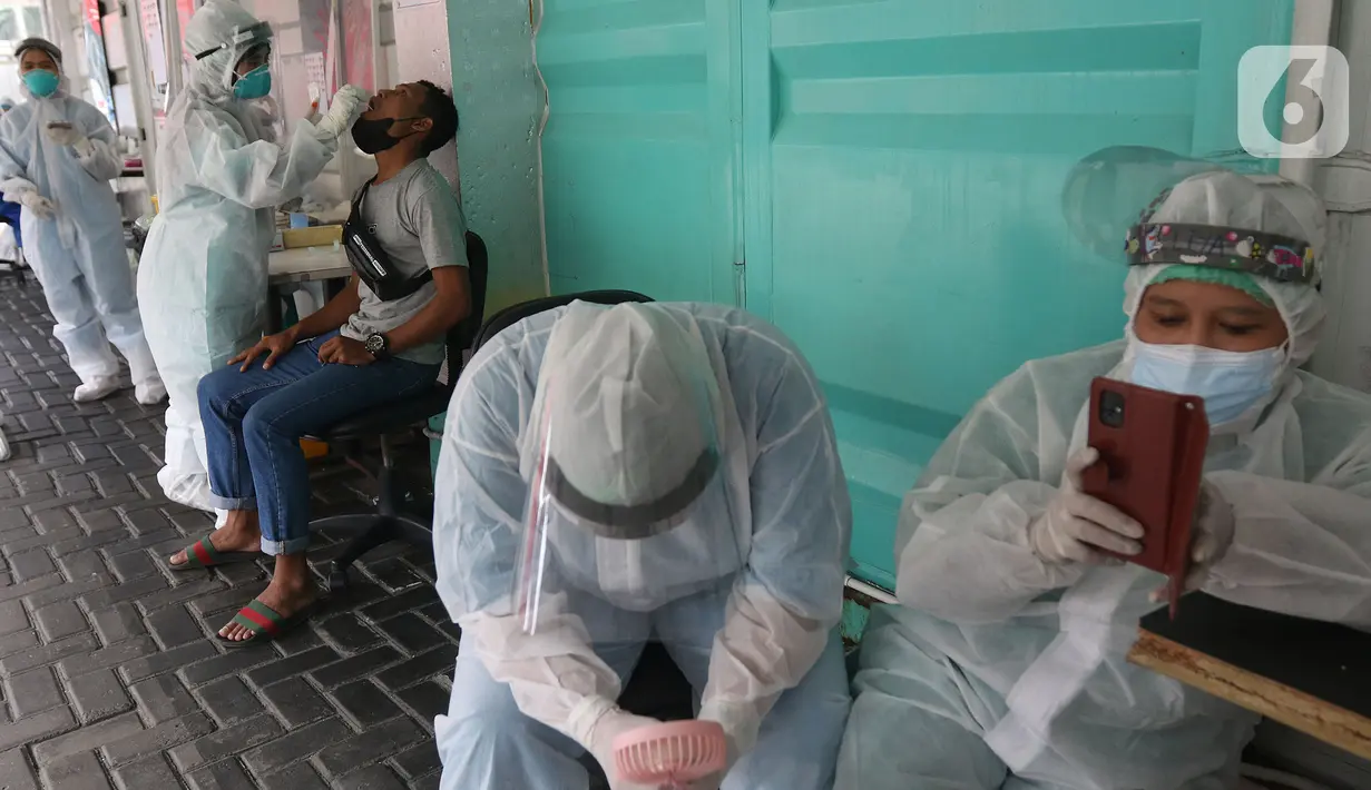Petugas kesehatan beristirahat ketika rekannya melakukan tes usap (swab test) PCR di Jakarta, Senin (25/10/2021). Presiden Joko Widodo atau Jokowi mengarahkan untuk menurunkan harga tes PCR menjadi Rp300 ribu dan masa berlaku diperpanjang 3x24 jam.  (Liputan6.com/Herman Zakharia)