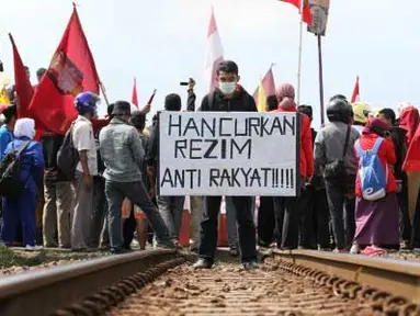Seorang demonstran membawa poster di tengah rel kereta api saat melakukan aksi memblokir jalur KA di Pintu perlintasan KA Stasiun Purwokerto, Banyumas, Jateng, Jumat (30/3). Mereka menolak rencana kenaikan BBM yang akan dilakukan pemerintah dengan cara memblokir jalur KA tersebut. (Antara)