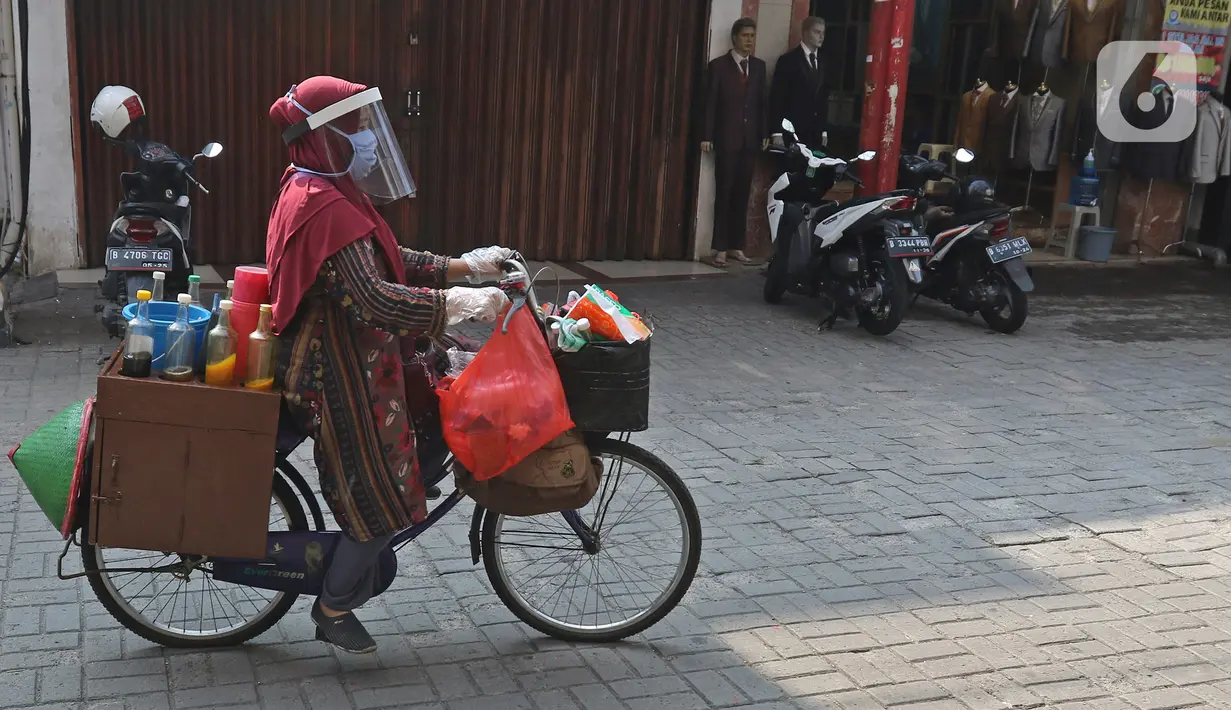 Tidar (46), mengayuh saat berjualan jamu di Pasar Baru, Jakarta, Kamis (11/06/2020). Penjual jamu tradisional keliling ini tampak mematuhi protokol kesehatan pencegahan COVID-19 dengan mengenakan masker, face shield, dan sarung tangan dalam melayani pelanggan setianya. (Liputan6.com/Herman Zakharia)