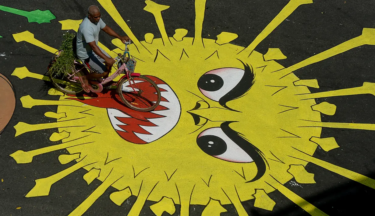 Pengendara motor melewati melewati grafiti virus corona yang dilukis di jalan selama penerapan lockdown nasional di Chennai, India, Senin (13/4/2020). Grafiti itu dibuat untuk meningkatkan kesadaran warga yang keluyuran keluar rumah saat lockdown karena pandemi virus corona. (Arun SANKAR/AFP)