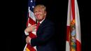 Capres AS dari Partai Republik, Donald Trump memeluk bendera AS saat melakukan kampanye menyapa pendukungnya di Tampa, Florida, AS (24/10). Trump akan bertarung dengan Hillary Clinton memperebutkan kursi di Gedung Putih. (REUTERS/Jonathan Ernst)