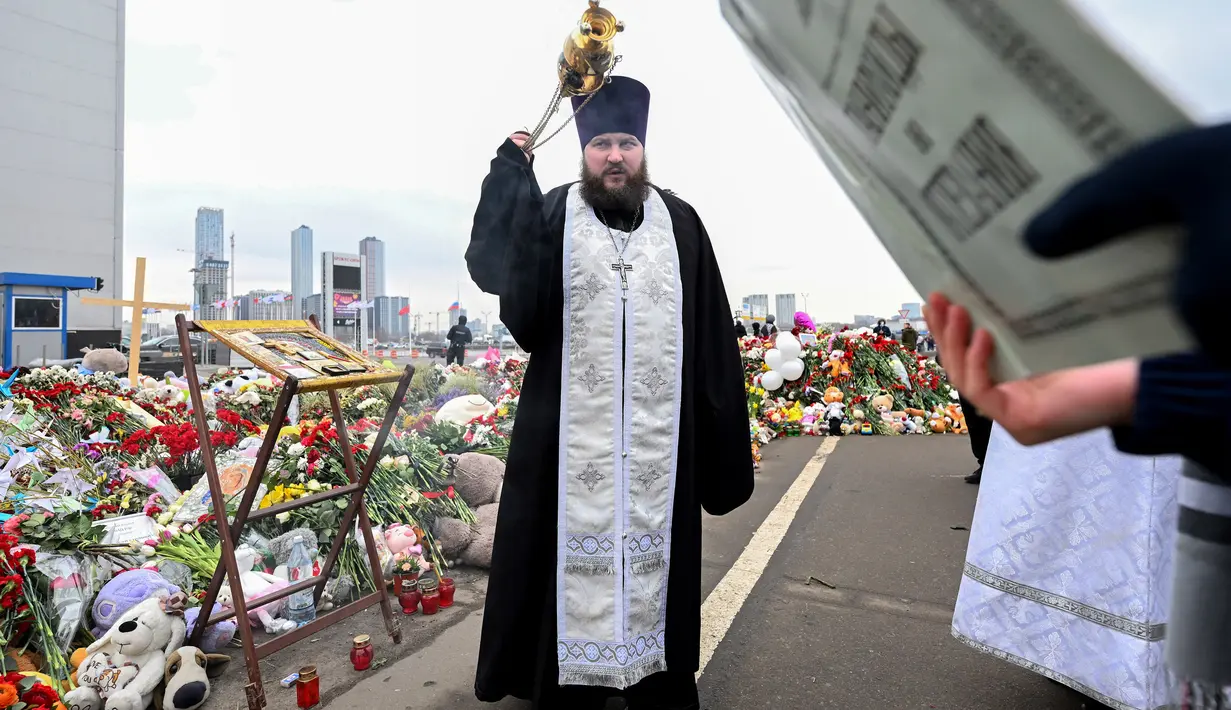 Seorang pendeta Ortodoks memimpin kebaktian di tugu peringatan di depan Balai Kota Crocus di pinggiran utara Moskow, Krasnogorsk, pada 29 Maret 2024. (NATALIA KOLESNIKOVA/AFP)