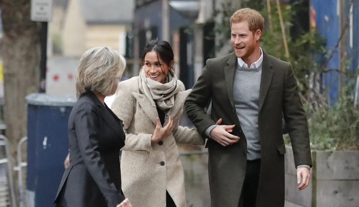 Pangeran Harry (kanan) dan Meghan Markle (tengah) berjalan sambil tertawa saat kunjungan ke stasiun radio Reprezent 107,3 FM di Brixton, London, Selasa, (9/1). (AP Photo/Dominic Lipinski, Pool)