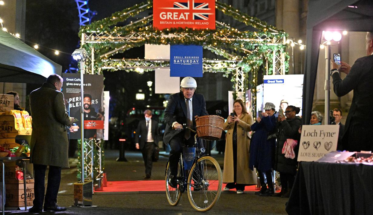 Perdana Menteri Inggris Boris Johnson mengendarai sepeda saat kunjungannya ke pasar Makanan dan Minuman Inggris yang didirikan di Downing Street, London, 30 November 2021. Sebanyak 12 bisnis dari seluruh Inggris memiliki kios untuk memamerkan produk mereka. (JUSTIN TALLIS/AFP/POOL)