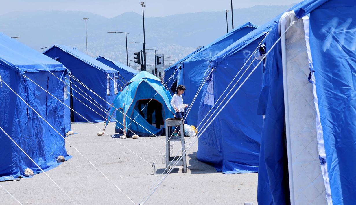 Seorang gadis Lebanon yang mengungsi berjalan di antara tenda-tenda biru yang didirikan pemerintah untuk orang-orang yang meninggalkan rumah dan desa mereka di pinggiran selatan Beirut dan Lebanon Selatan, Jumat 22 Mei 2026. (Anwar AMRO/AFP)