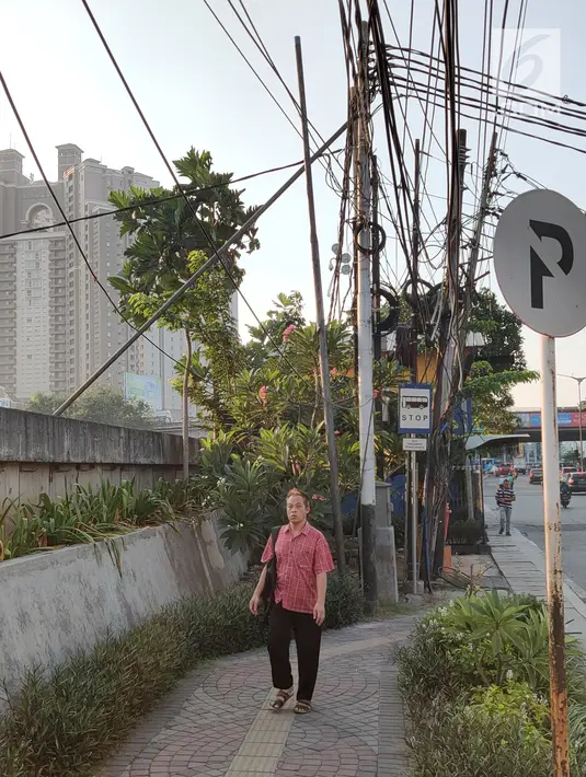 Pejalan kaki melintas di bawah kabel semrawut di sekitar Jalan Gunung Sahari, Mangga Dua, Jakarta, Kamis (10/7/2019). Buruknya tata instalasi kabel di Ibu Kota menjadi penyebab banyaknya kabel semrawut, meskipun kondisi itu berbahaya serta mengganggu pemandangan. (Liputan6.com/Immanuel Antonius)