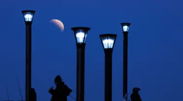 Sejumlah pria berdiri di bawah lampu jalan ketika fenomena gerhana bulan sebagian (parsial) di Buenos Aires, Argentina, Selasa (16/7/2019). Gerhana bulan parsial ini bisa diamati dari Amerika Selatan, Eropa, Afrika, Asia dan Australia. (AP Photo/Natacha Pisarenko)