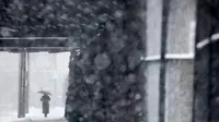 Seorang wanita menggunakan payung berjalan di bawah salju lebat saat terjadi badai salju di Hoboken, New Jersey (21/3). Karena badai salju yang melanda New Jersey ini layanan komuter dan bus dihentikan pada pukul 3 sore. (AP/Julio Cortez)