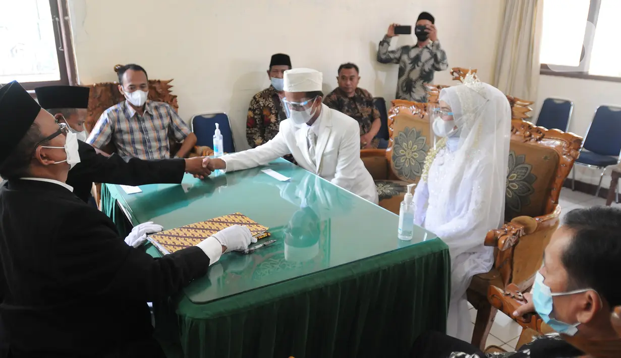 Pengantin pria menggunakan masker mengucapkan kalimat ijab-kabul saat prosesi pernikahan di KUA Pamulang, Tangerang Selatan, Selasa (22/2/2022). Sebanyak 10 pasangan menjalankan akad nikah di KUA Pamulang pada hari ini yang dianggap memiliki tanggal cantik. (merdeka.com/Arie Basuki)