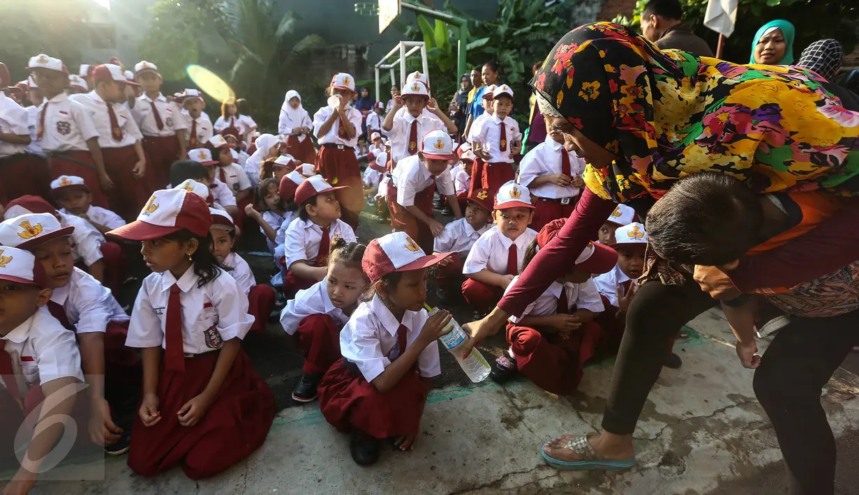 Orangtua memberikan minum pada anaknya sebelum upacara pada hari pertama sekolah di SDN Pasar Baru 05 Jakarta, Senin (18/7). Usai libur Idul Fitri, para siswa kembali mengikuti pelajaran di sekolah untuk tahun ajaran 2015-2016 (Liputan6.com/Faizal Fanani)
