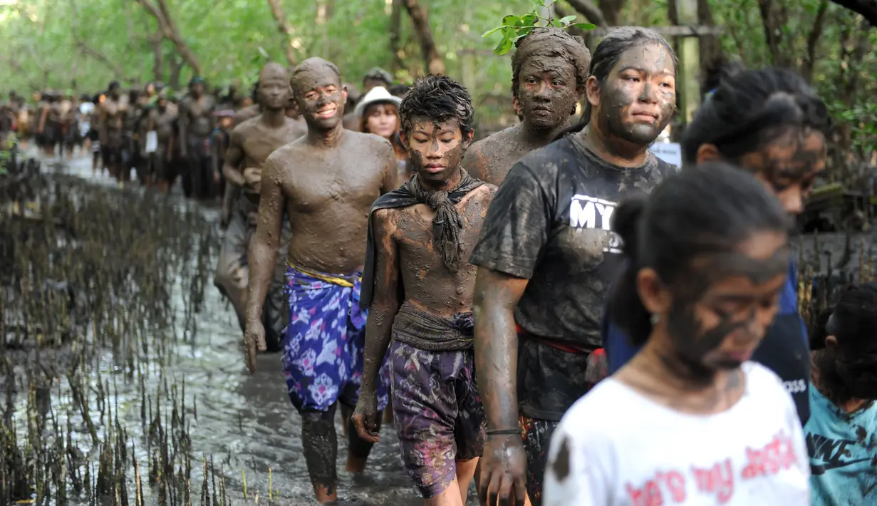 Warga Bali berjalan bersama dengan badan penuh lumpur saat mengikuti mandi lumpur tradisional atau yang dikenal sebagai Mebuug-buugan di desa Kedonganan, Bali (18/3). (AFP/Sony Tumbelaka)