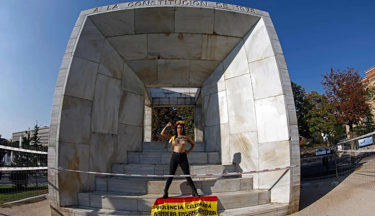 Aktivis perempuan Femen menuliskan "Illegitimate flag" di dadanya dan membawa bendera Spanyol bertuliskan 'Celebrated violence bloody flag' saat unjuk rasa di monumen Konstitusi Spanyol 1978 di Madrid, (11/10). (AFP Photo/Oscar Del Pozo)