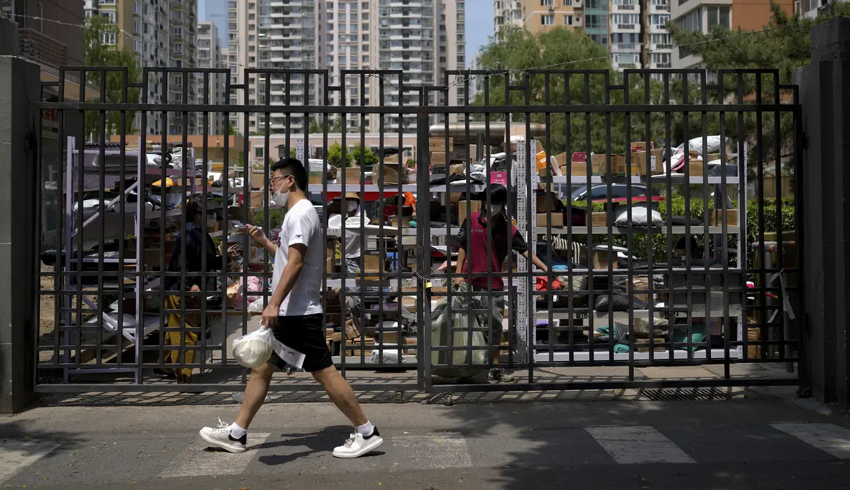 Seorang penduduk berjalan ketika pekerja pengiriman memilah paket di tempat pengumpulan di luar apartemen setelah pihak berwenang melarang mereka memasuki tempat itu karena peraturan pembatasan sosial Covid-19 di Beijing pada Senin, 23 Mei 2022. Beijing memperpanjang perintah bagi pekerja dan siswa untuk tinggal di rumah dan memerintahkan pengujian massal tambahan pada hari Senin untuk membendung kasus COVID-19 yang kembali meningkat di ibu kota China. (AP Photo/Andy Wong)