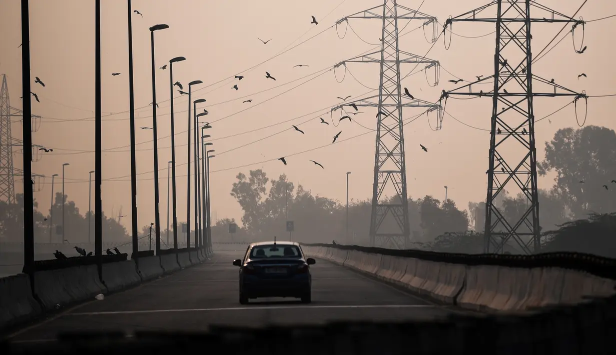 Seorang pengendara mobil mengemudi di sepanjang jalan di tengah kondisi asap tebal yang menyelimuti sehari setelah perayaan Diwali, festival cahaya Hindu, di New Delhi, India pada Minggu (15/11/2020). (Photo by Sajjad HUSSAIN / AFP)