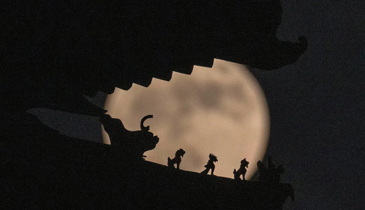 Dekorasi atap pada menara sudut Kota Terlarang menggambarkan siluet binatang suci terhadap bulan purnama di Beijing, China, 14 Juni 2022. Fenomena ini disebut juga sebagai Strawberry Supermoon karena terjadi pada saat panen strawberry. (AP Photo/Ng Han Guan)