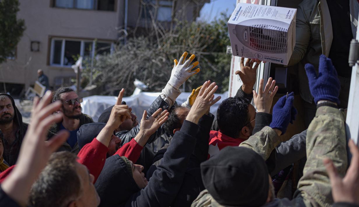 Warga mengambil makanan, pakaian, dan barang-barang rumah tangga yang dikirim dari bagian belakang truk di Samandag, selatan Hatay pada 16 Februari 2023, sepuluh hari setelah gempa berkekuatan magnitudo 7,8 melanda wilayah perbatasan Turki dan Suriah. Lusinan tangan dengan panik meraih pemanas dan selimut yang dibagikan oleh donor swasta, menggambarkan keputusasaan dan kemarahan yang mencengkeram wilayah Turki 11 hari setelah bencana gempa. (Photo by Yasin AKGUL / AFP)