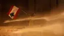 Demonstran antipemerintah mengibarkan bendera Lebanon saat dia disemprot air dalam demonstrasi menentang pemerintahan baru dekat Parliament Square, Beirut, Lebanon, Rabu (22/1/2020). Demonstrasi dan kekerasan terus berlanjut kendati Lebanon telah mengumumkan kabinet baru. (AP Photo/Hussein Malla)