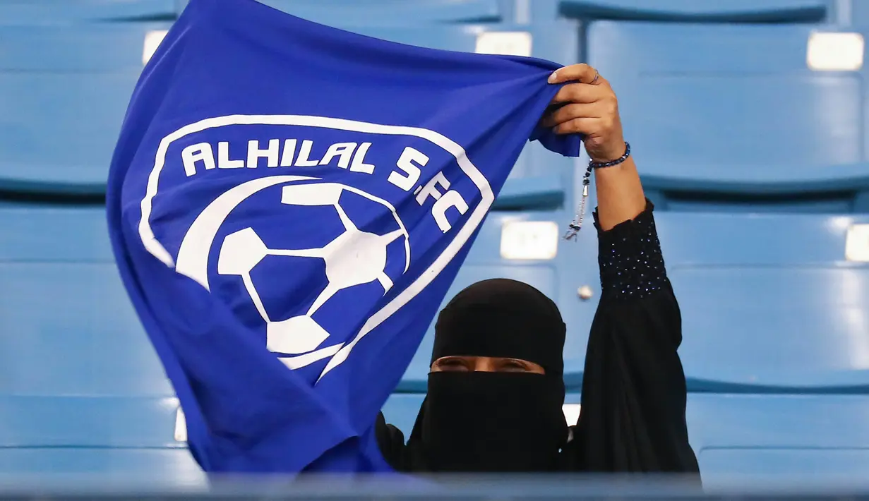 Seorang wanita mengibarkan bendera saat mendukung tim Al-Hilal dari Saudi melawan Al-Ittihad dalam pertandingan Liga Saudi Pro di King Fahd International Stadium di Riyadh (13/1). (AFP Photo/Ali Al-Arifi)
