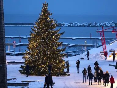 Orang-orang berjalan mengelilingi pohon cemara yang dihias untuk perayaan Natal dan Tahun Baru di Pelabuhan Noblessner, Teluk Tallinn, Estonia, 16 Desember 2023. (AP Photo/Pavel Golovkin)